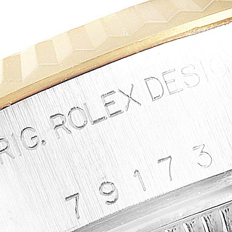 The image shows an angled close-up of the case side and bezel of a Rolex Datejust 79173 Women's Steel and Gold (two tone) White Dial 79173 Women's Steel and Gold (two tone) White Dial watch with engraved text.