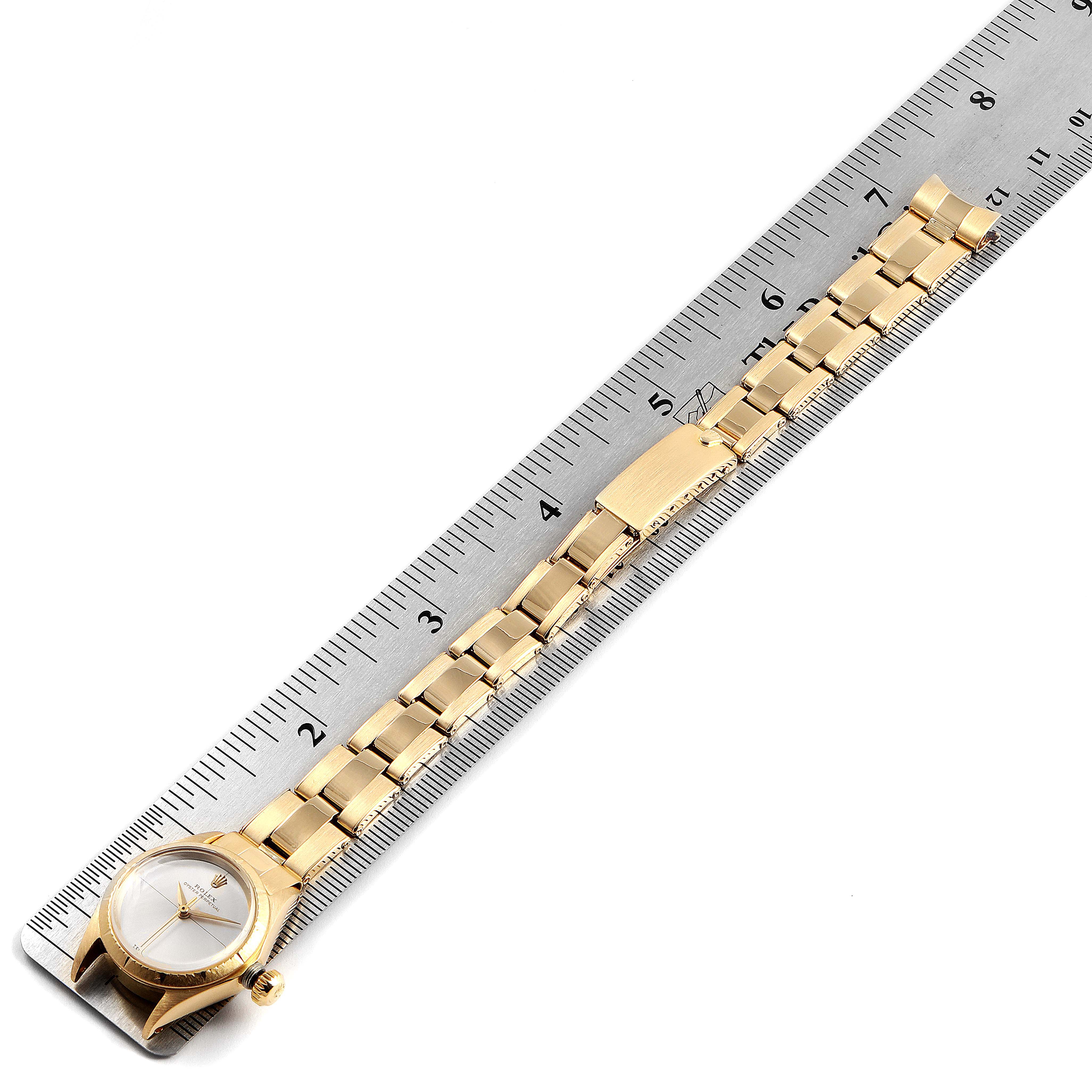 This image shows a top-down view of a Rolex Oyster Perpetual 6615 Women's Yellow Gold Silver Dial 6615 Women's Yellow Gold Silver Dial watch with its gold bracelet aligned to a ruler for scale.