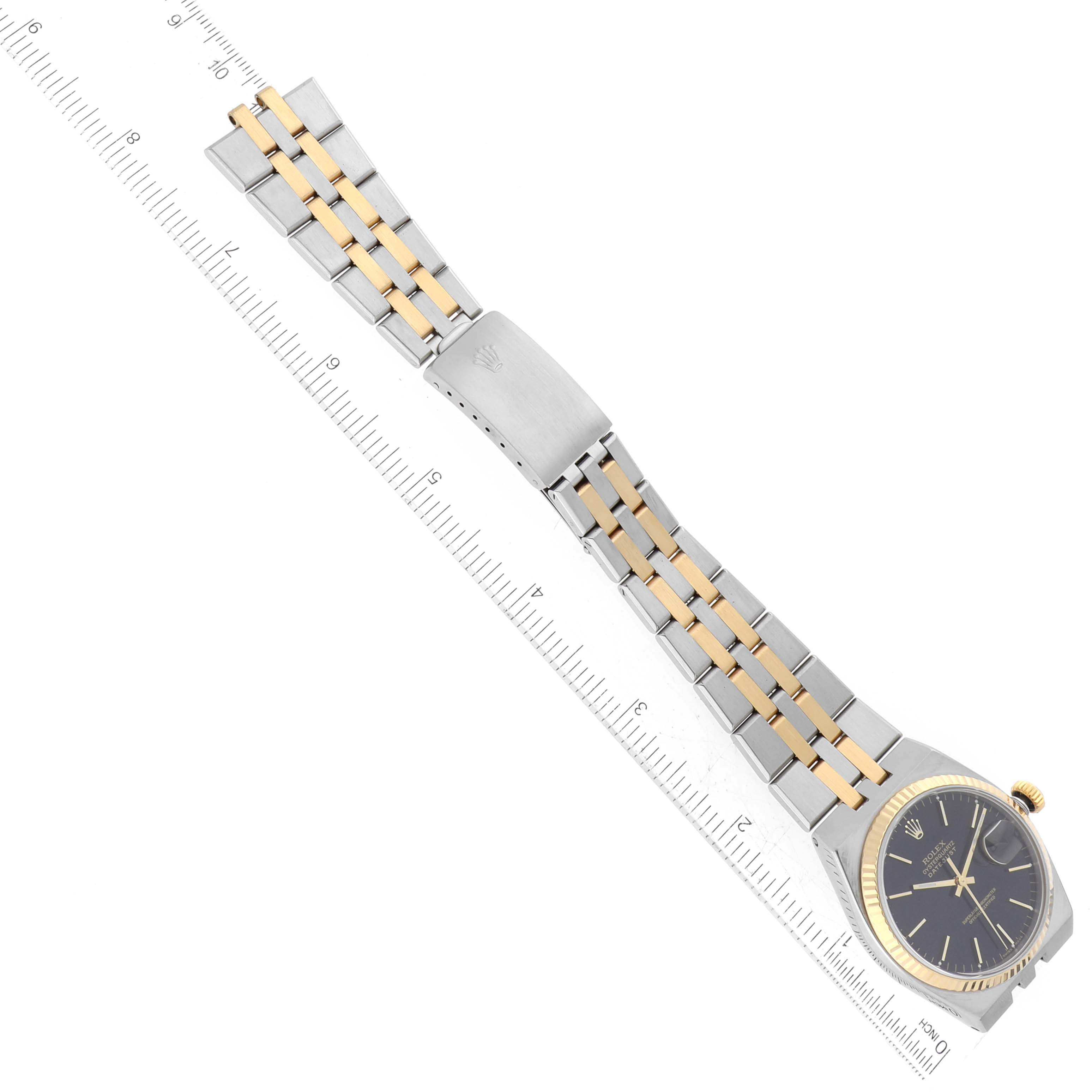 The Rolex Oysterquartz 17013 Men's Steel and Gold (two tone) Black Dial 17013 Men's Steel and Gold (two tone) Black Dial watch is shown laid flat, featuring the full bracelet, clasp, and dial, with a ruler for scale.